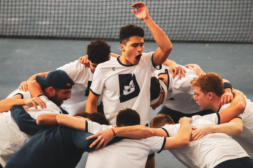 Nuoret tennisjoukkueet kokoontuvat ympyrässä, kun yksi pelaaja johtaa energistä huutoa ennen peliä.